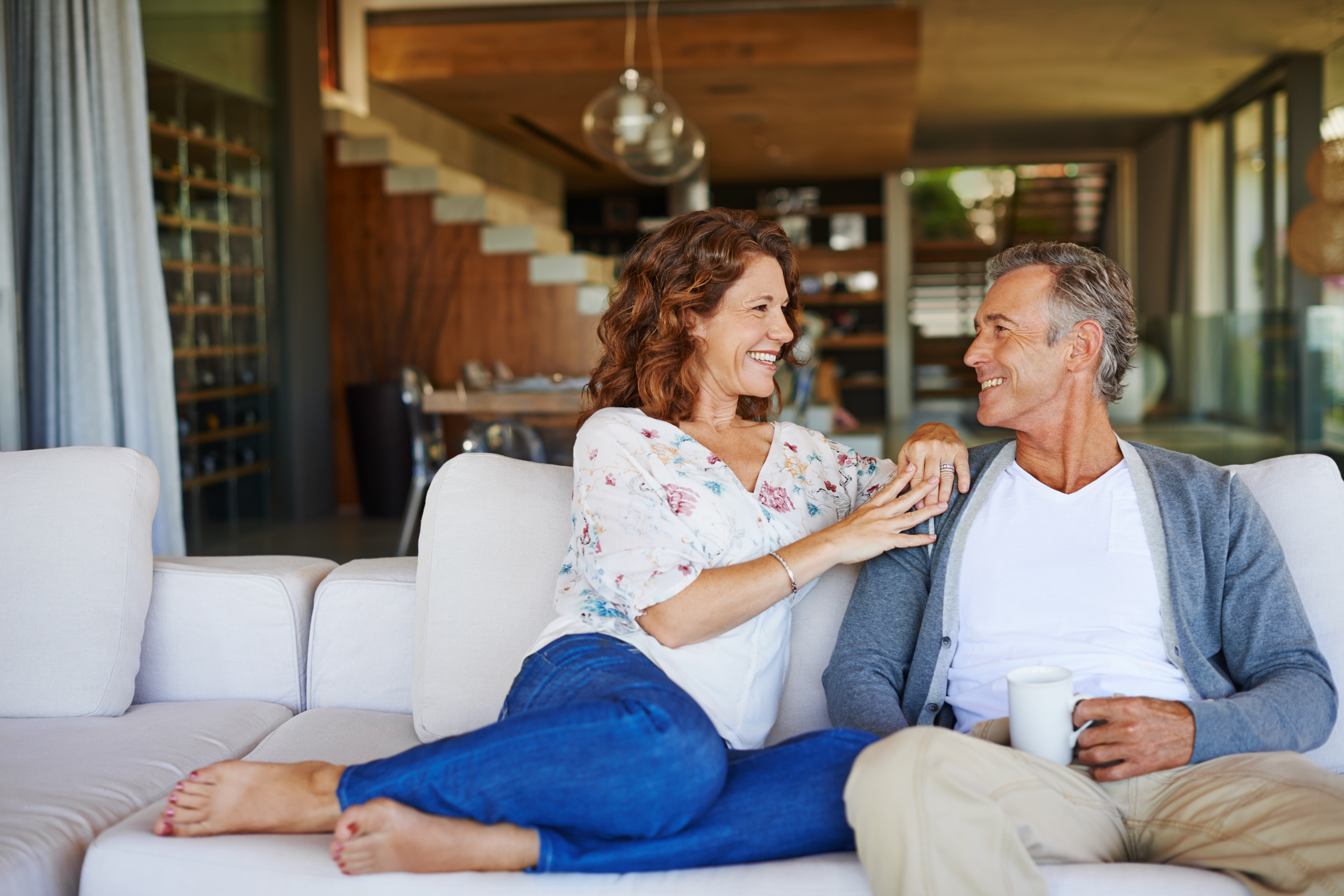 A couple sit together on a sofa, smiling at each other