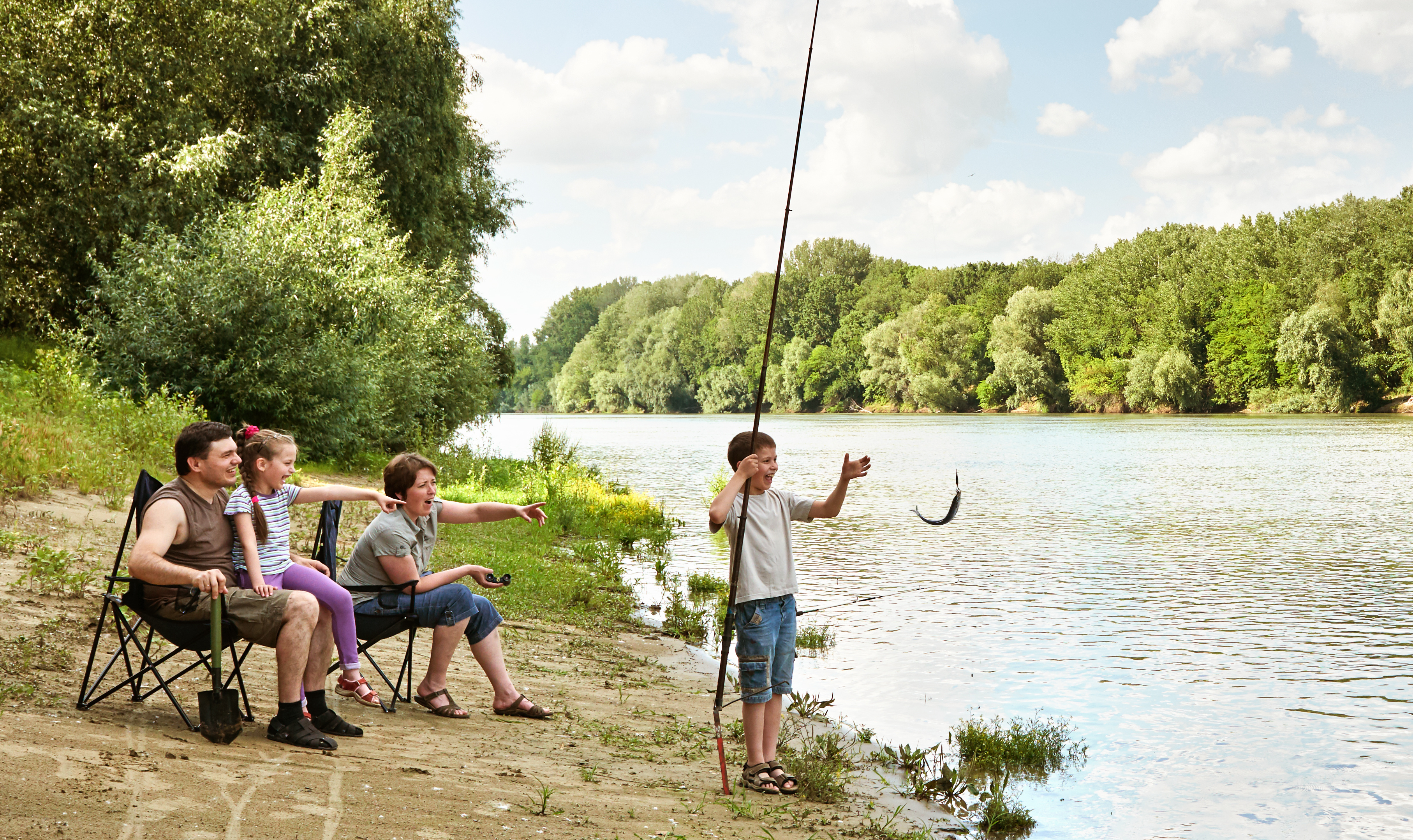 A family cheers as a boy holds up a fish on a riverbank