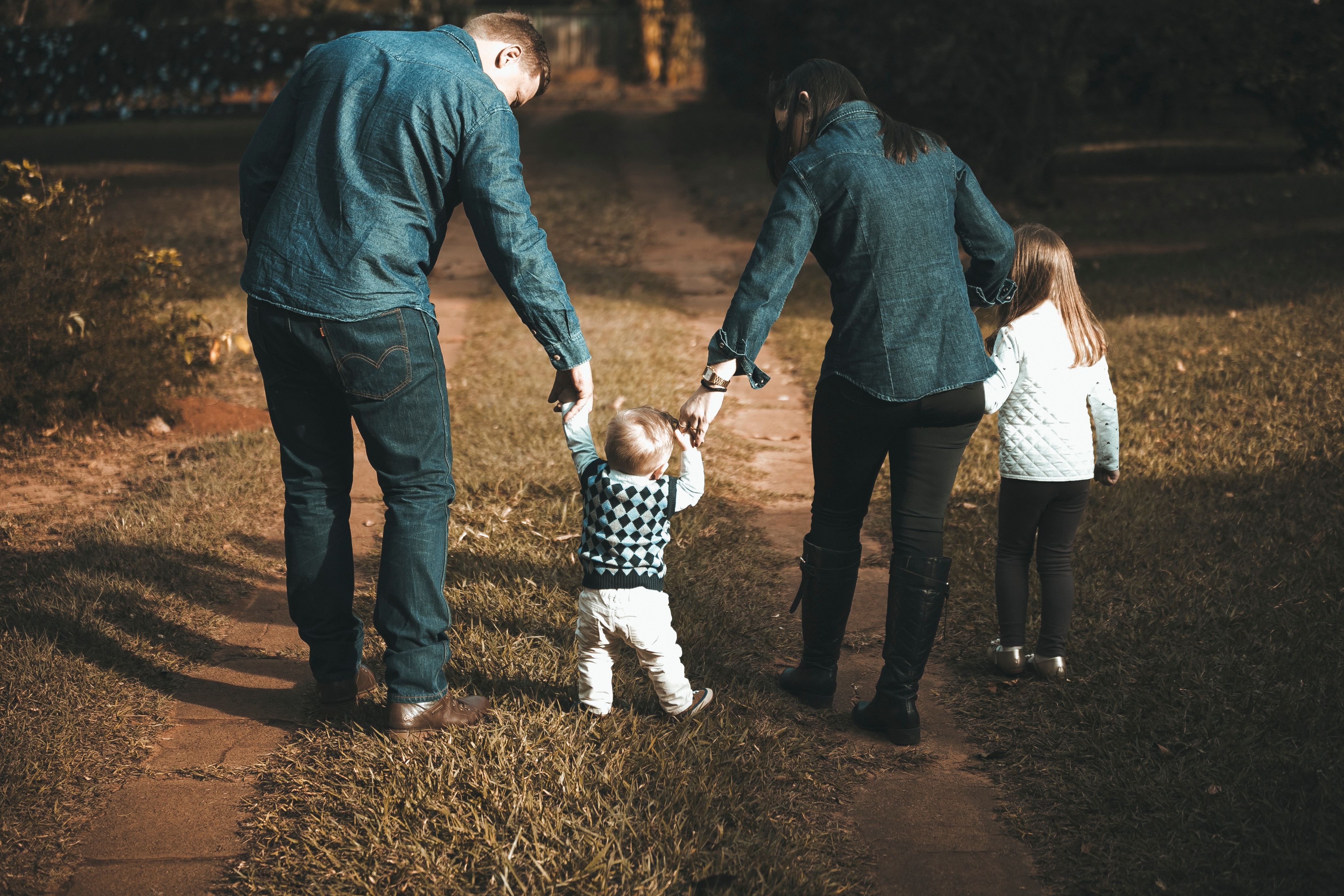A family of four walks hand in hand along a grassy path